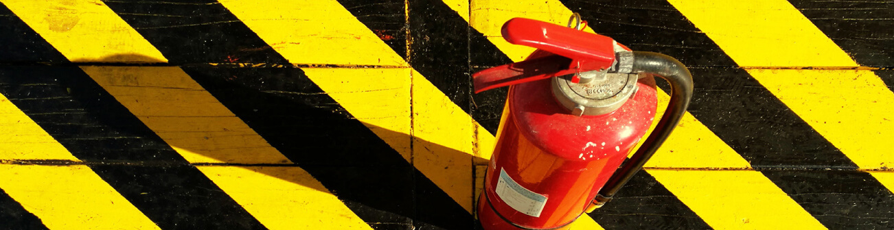 A red fire extinguisher on a surface with black and yellow hazard stripes.