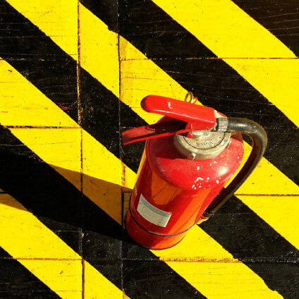 A red fire extinguisher on a surface with black and yellow hazard stripes.